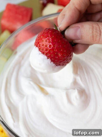 A hand holding a fresh strawberry dipped in fluffy marshmallow fruit dip.