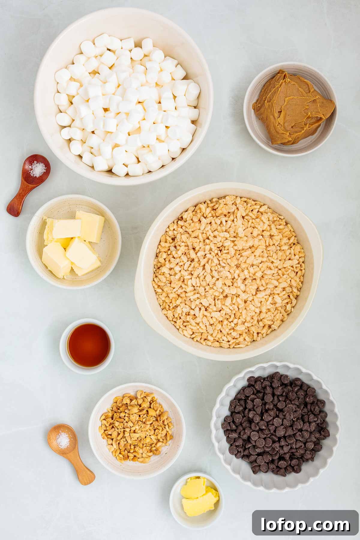 Chocolate Peanut Butter Rice Krispie Treat Recipe 3 Flat lay of measured ingredients in bowls for making Rice Krispie treats, including mini marshmallows, butter, peanut butter, vanilla, chopped peanuts, chocolate chips, and crispy rice cereal.