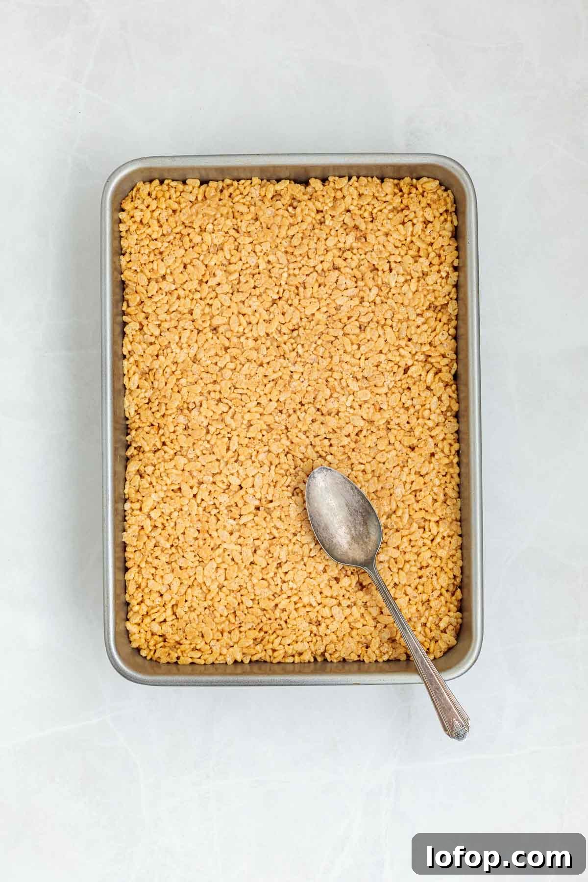 Chocolate Peanut Butter Rice Krispie Treat Recipe 7 Rice Krispie mixture pressed evenly into a metal baking pan with the back of a spoon resting on top, ready to be topped or cooled.