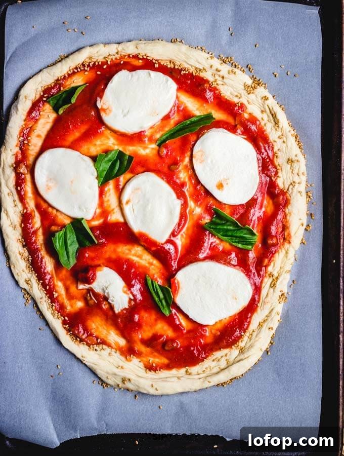 The garlicky tomato sauce, fresh mozzarella, and basil on the rolled out store bought pizza dough.
