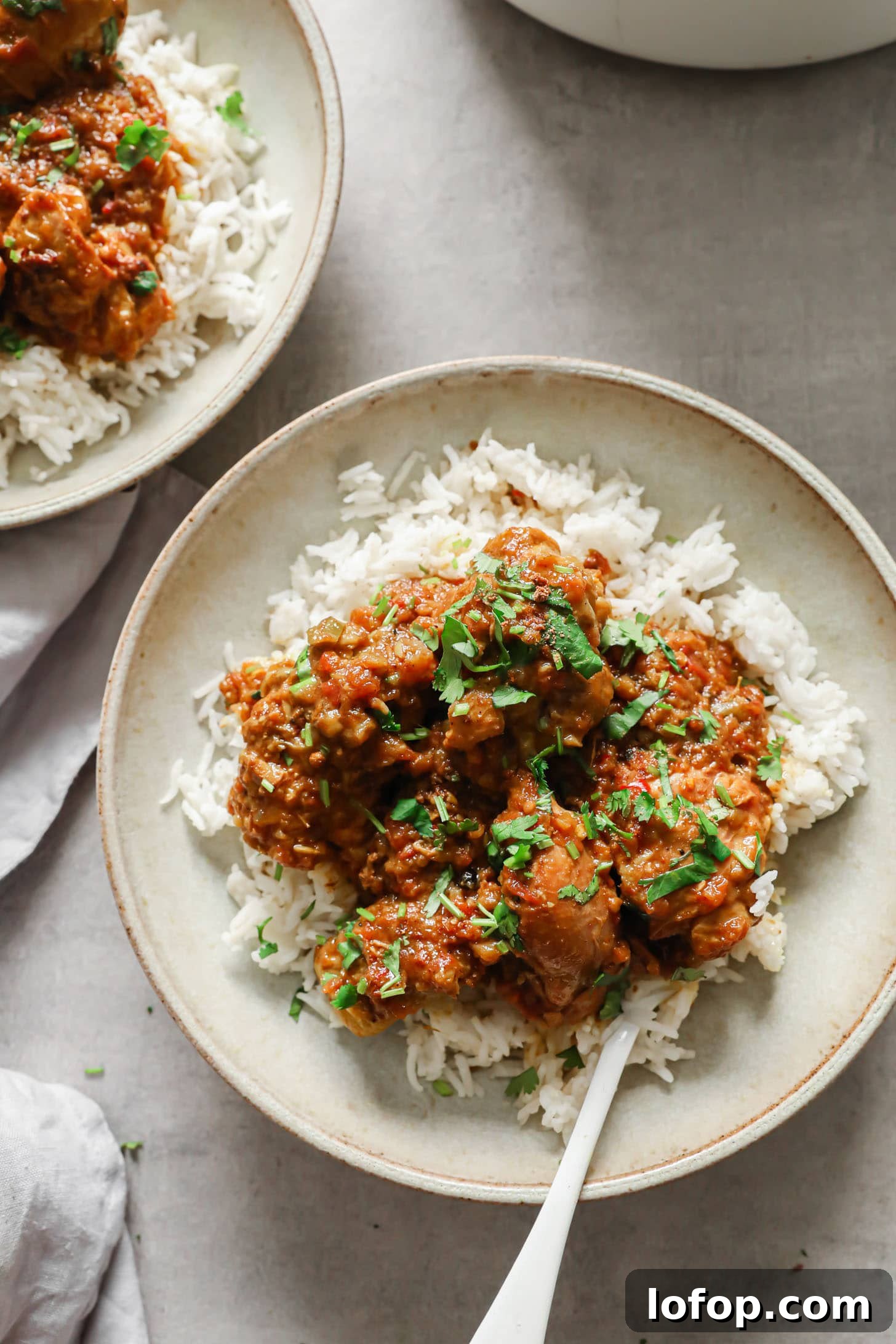 Chicken Curry served on top of basmati rice n a beige bowl with a white spoon