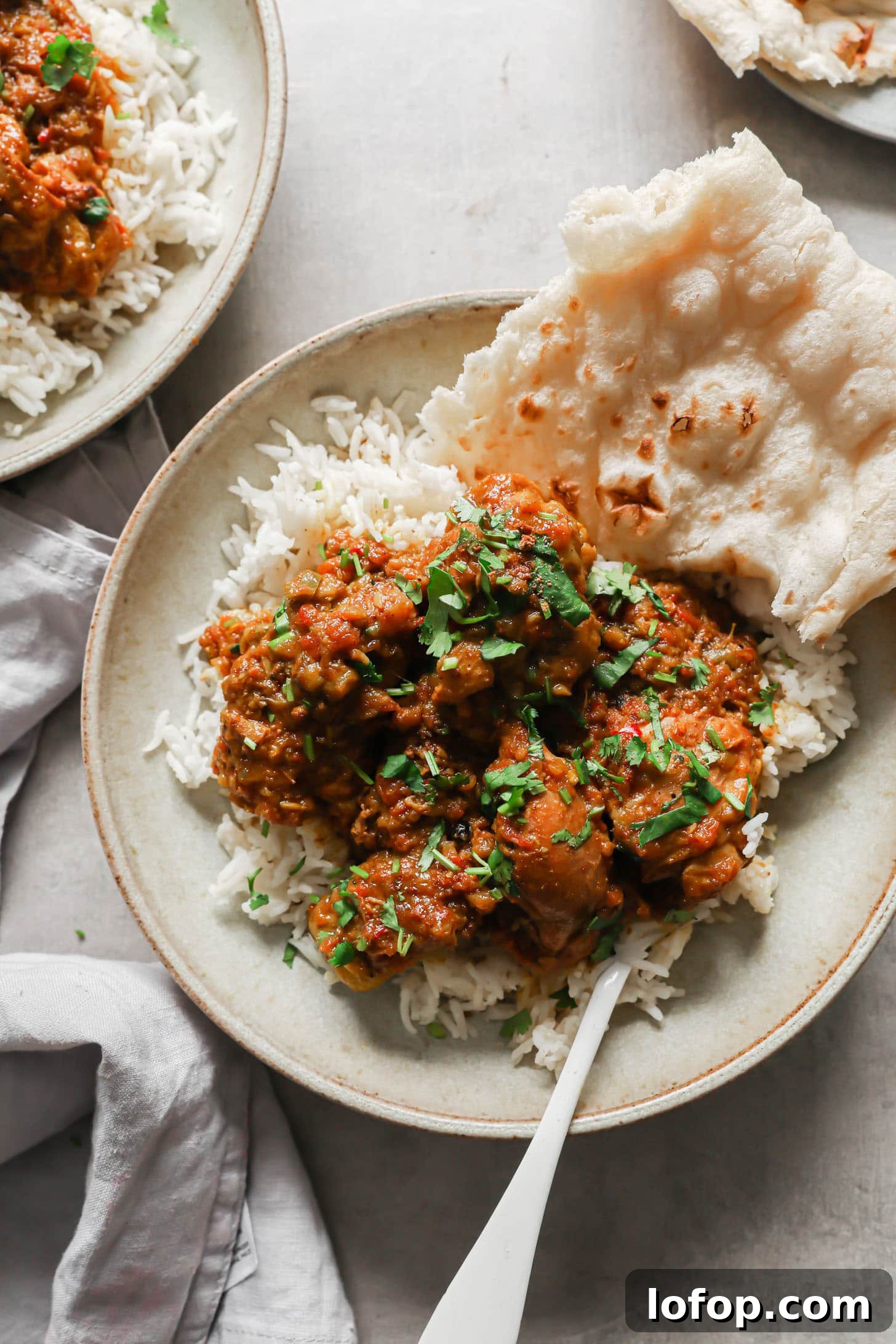 A bowl with chicken curry atop basmati rice with naan on the side