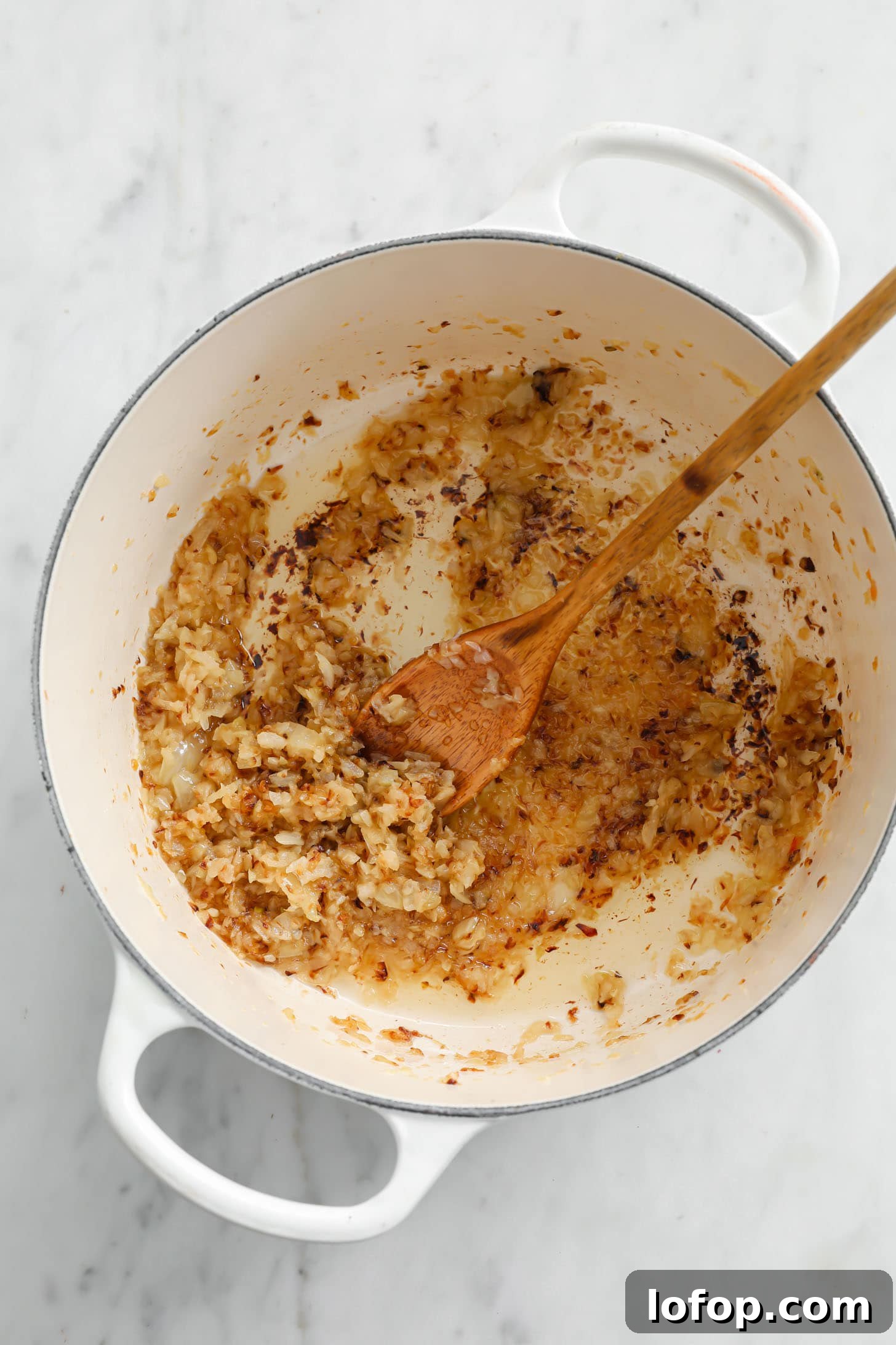 Browned onions in a Dutch oven with a wooden spatula