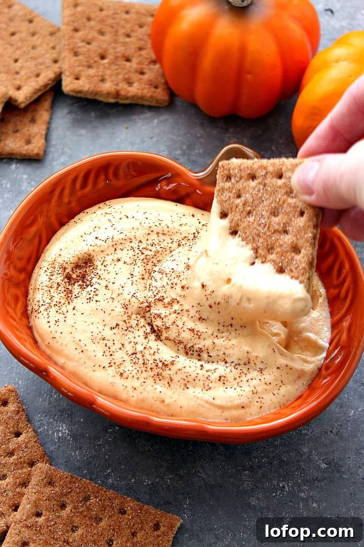Easy Pumpkin Cheesecake Dip - sweet and creamy dip that tastes just like pumpkin cheesecake! No whipped topping needed! Side shot of pumpkin cheesecake dip in pumpkin dish with cracker dipped in dip.