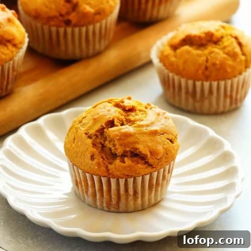 Square photo of a pumpkin muffin on a petal plate with more muffins in the background.