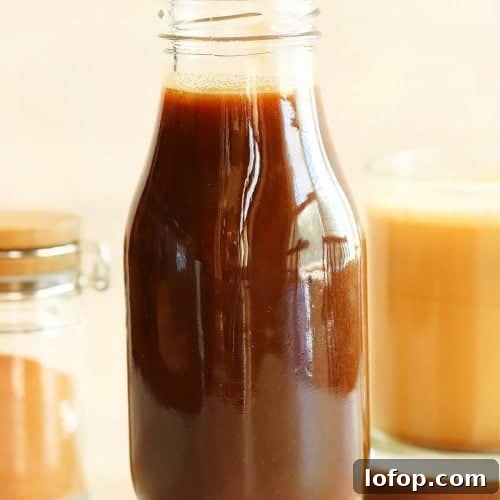 Square photo of pumpkin syrup in a glass bottle with a mug with coffee in the background.
