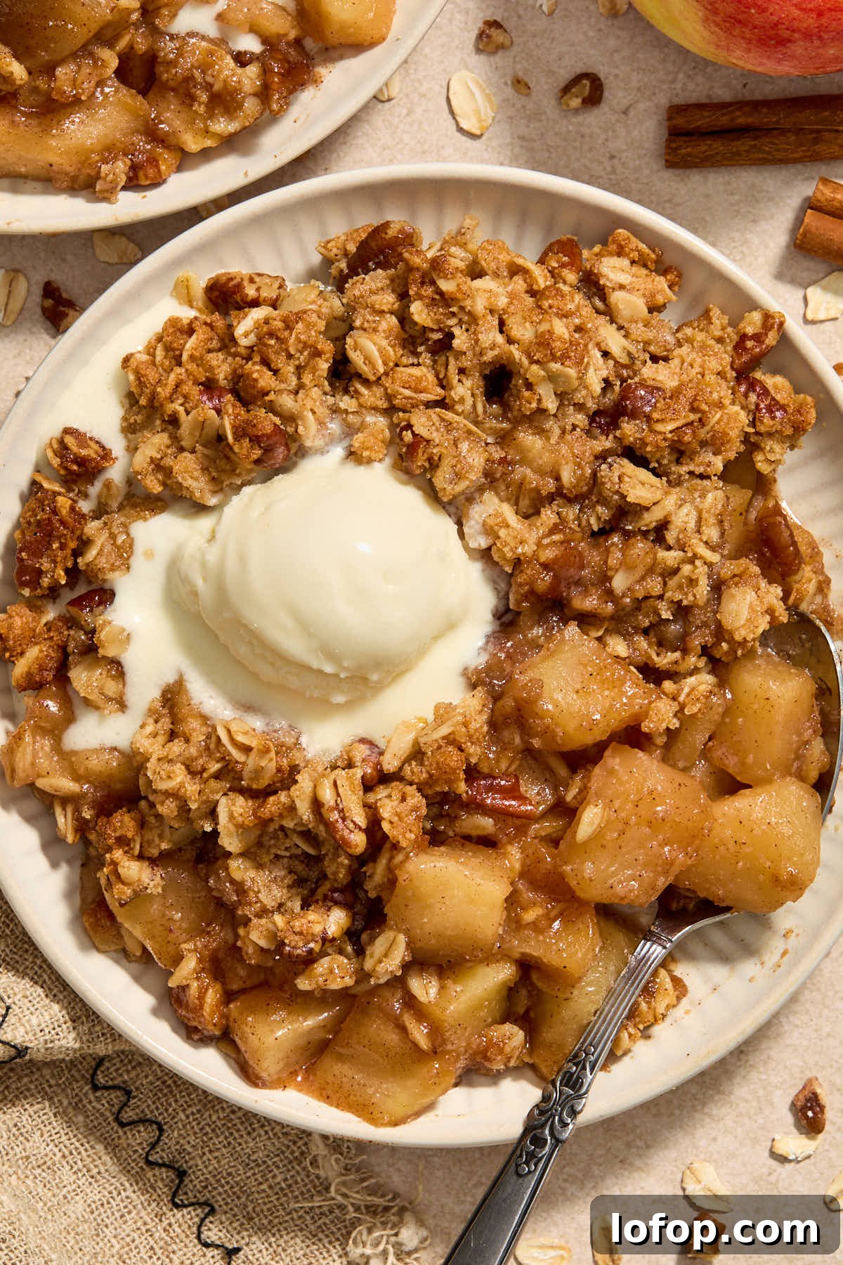 Serving of apple crisp on a plate with melted ice cream on top.