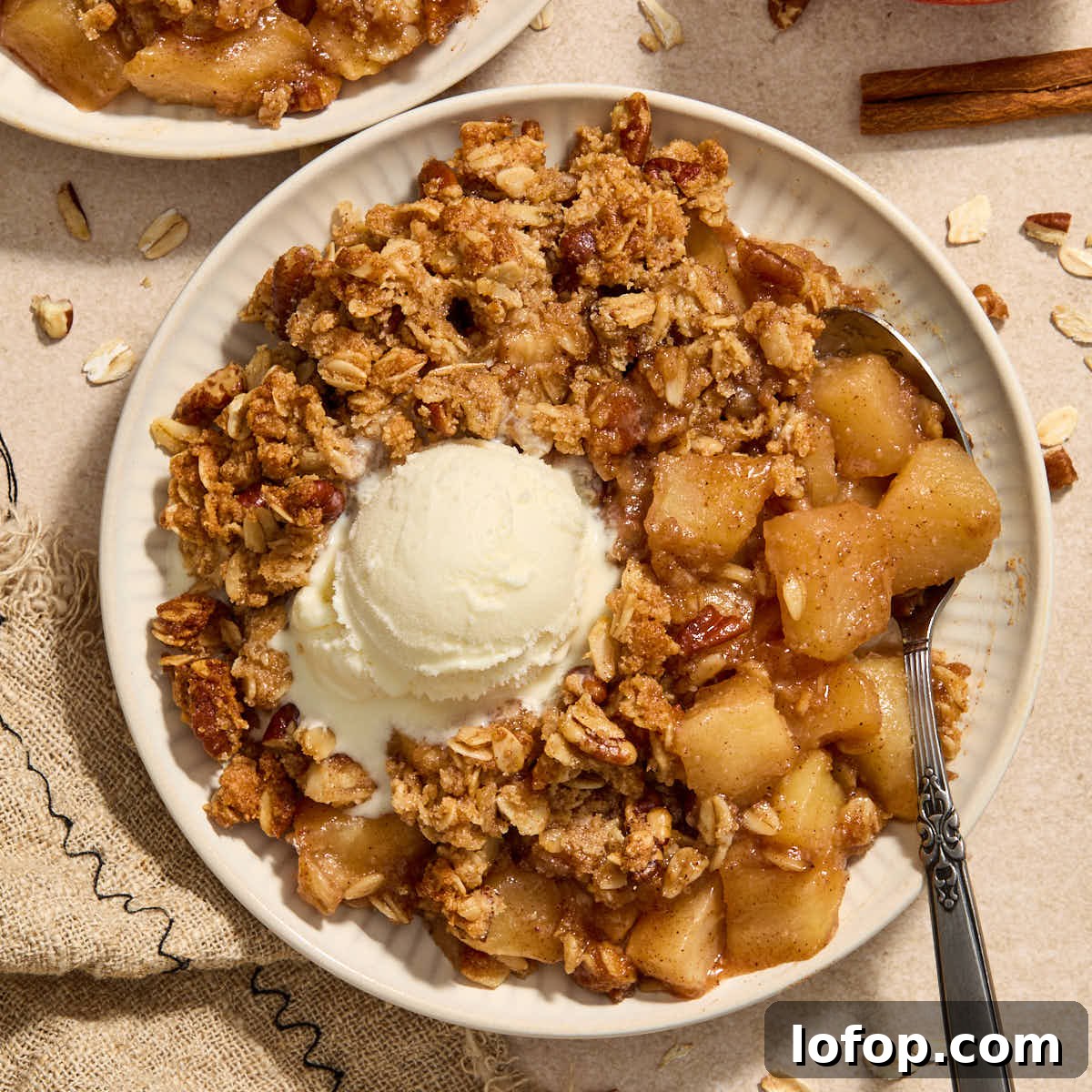 Almond flour apple pecan crisp served on a plate with a spoon and scoop of ice cream.