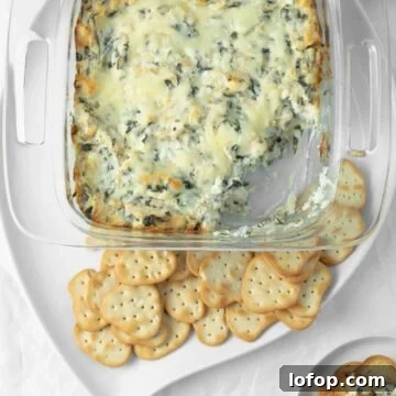 Baked spinach artichoke dip with a scoop taken out of it with crackers on a serving dish.