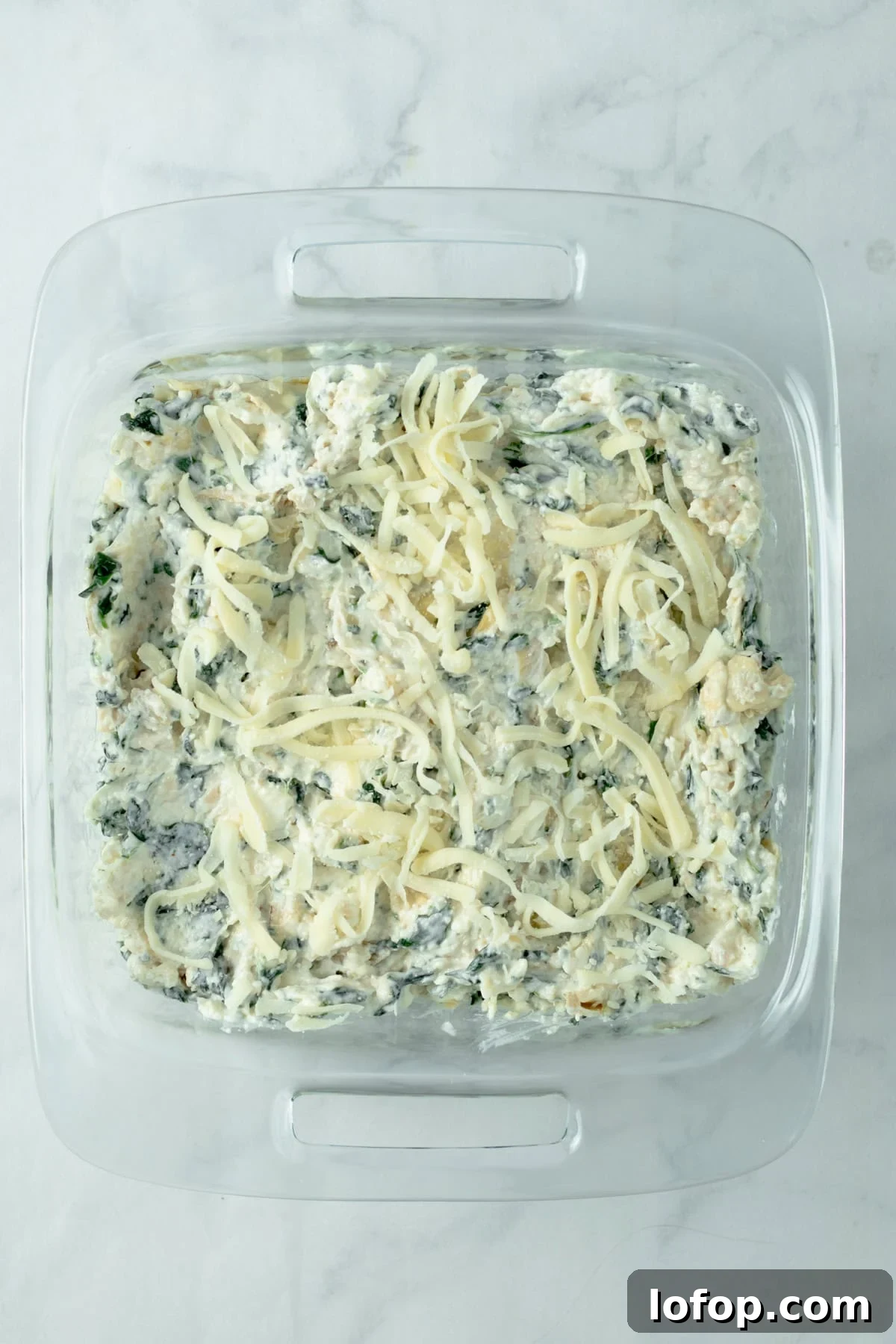 raw spinach artichoke dip topped with mozzarella in a glass baking dish.