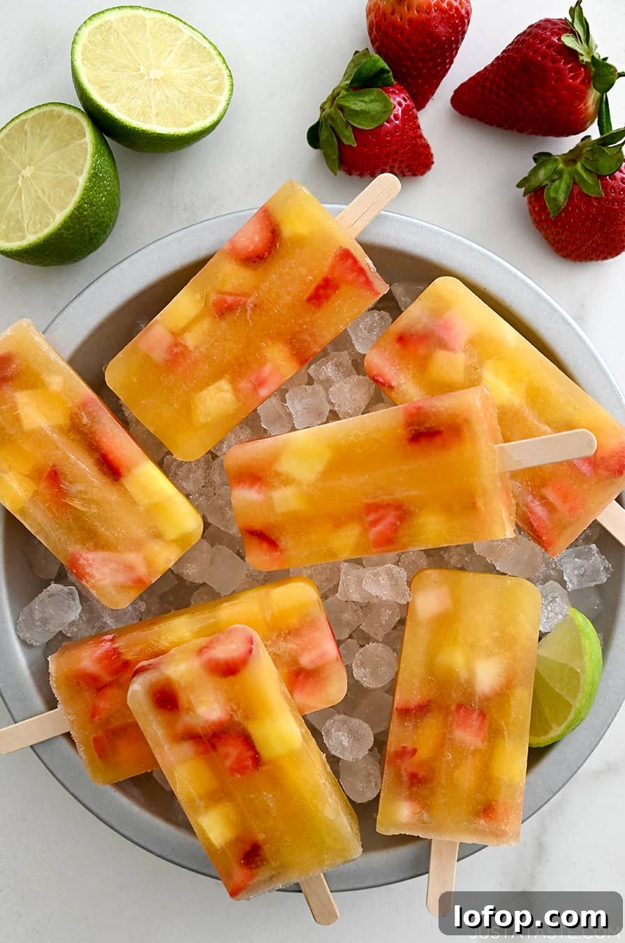 Peach Sangria Popsicles Recipe: Refreshing Boozy Summer Treat 8 A top-down view of Peach Sangria Popsicles over ice in a pie plate next to fresh strawberries and a lime cut open in half