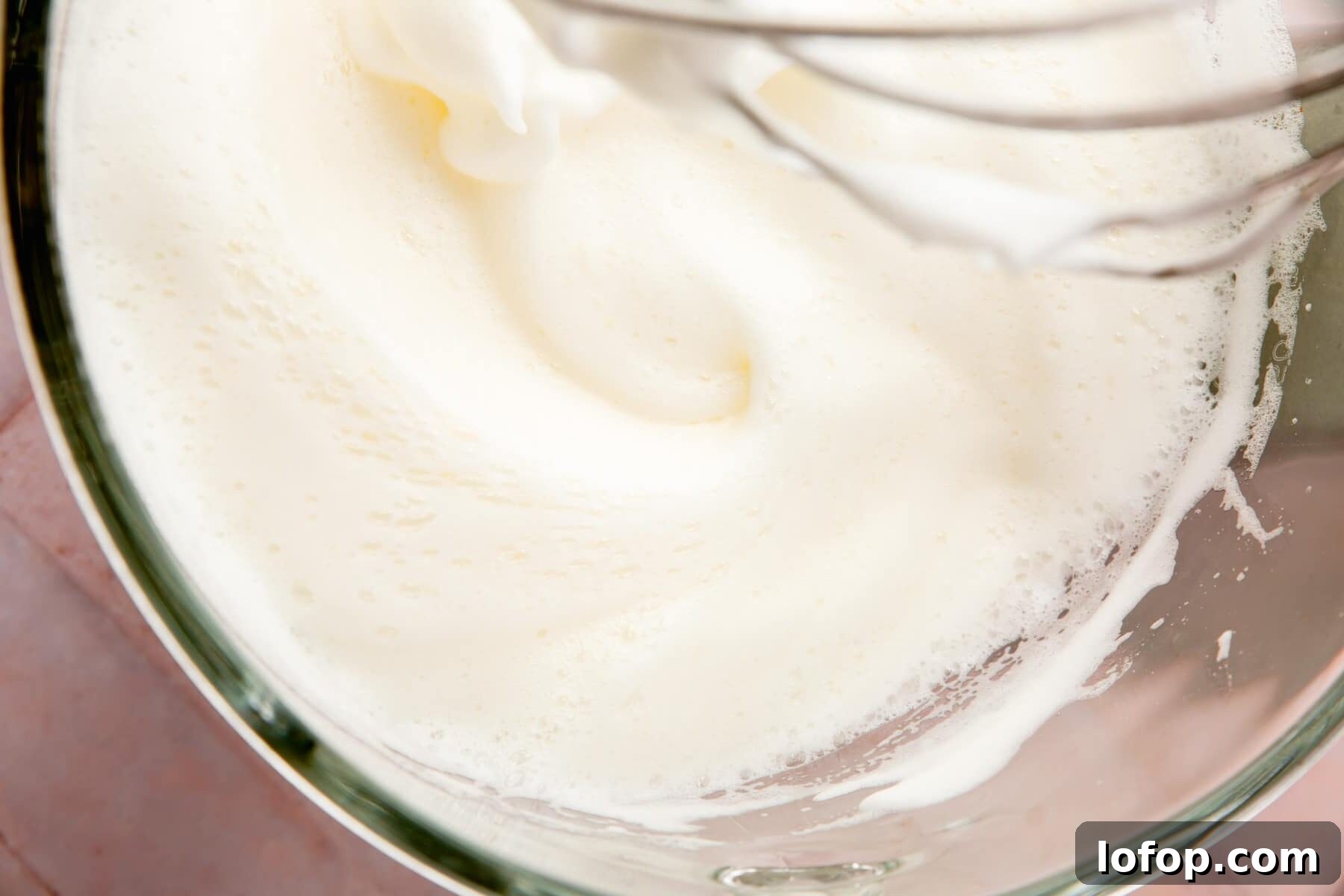 Egg whites and cream of tartar being whipped in a stand mixer.