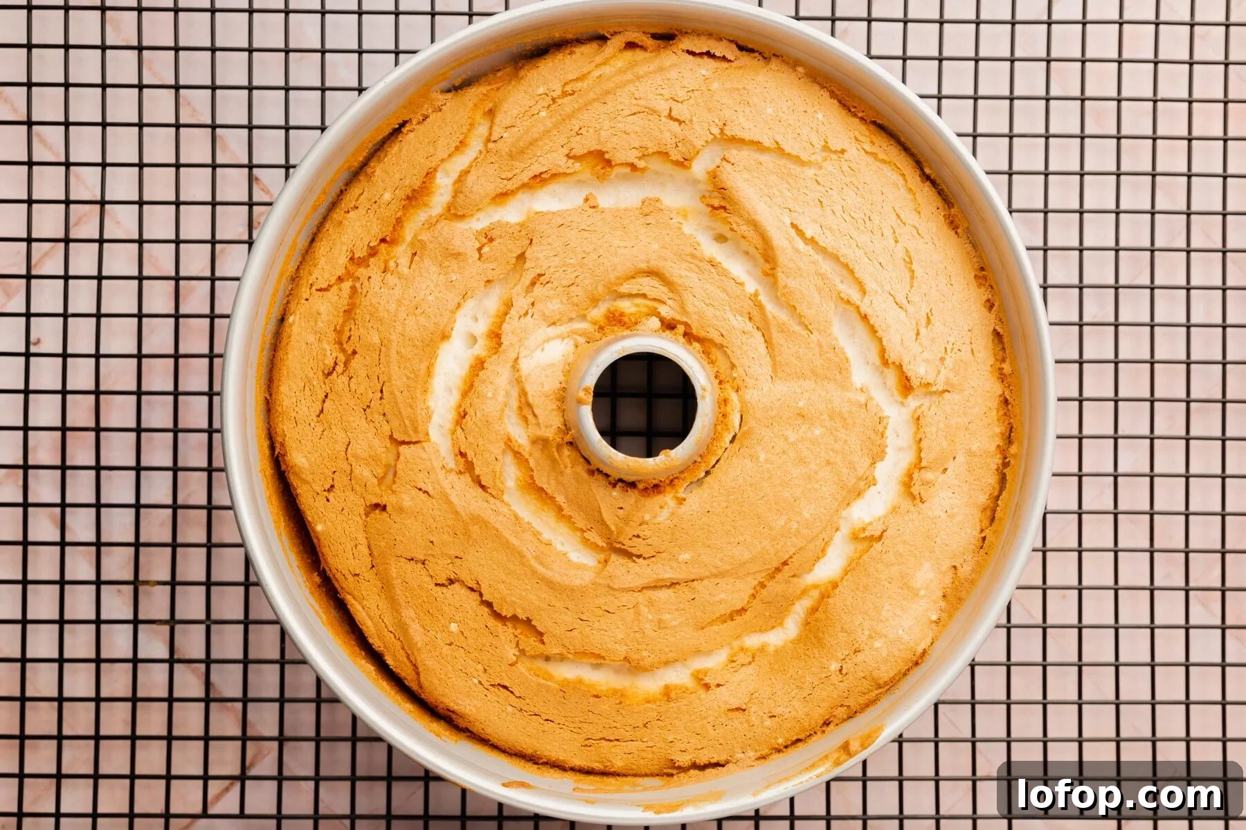 Angel food cake in a tube pan on a cooling rack.
