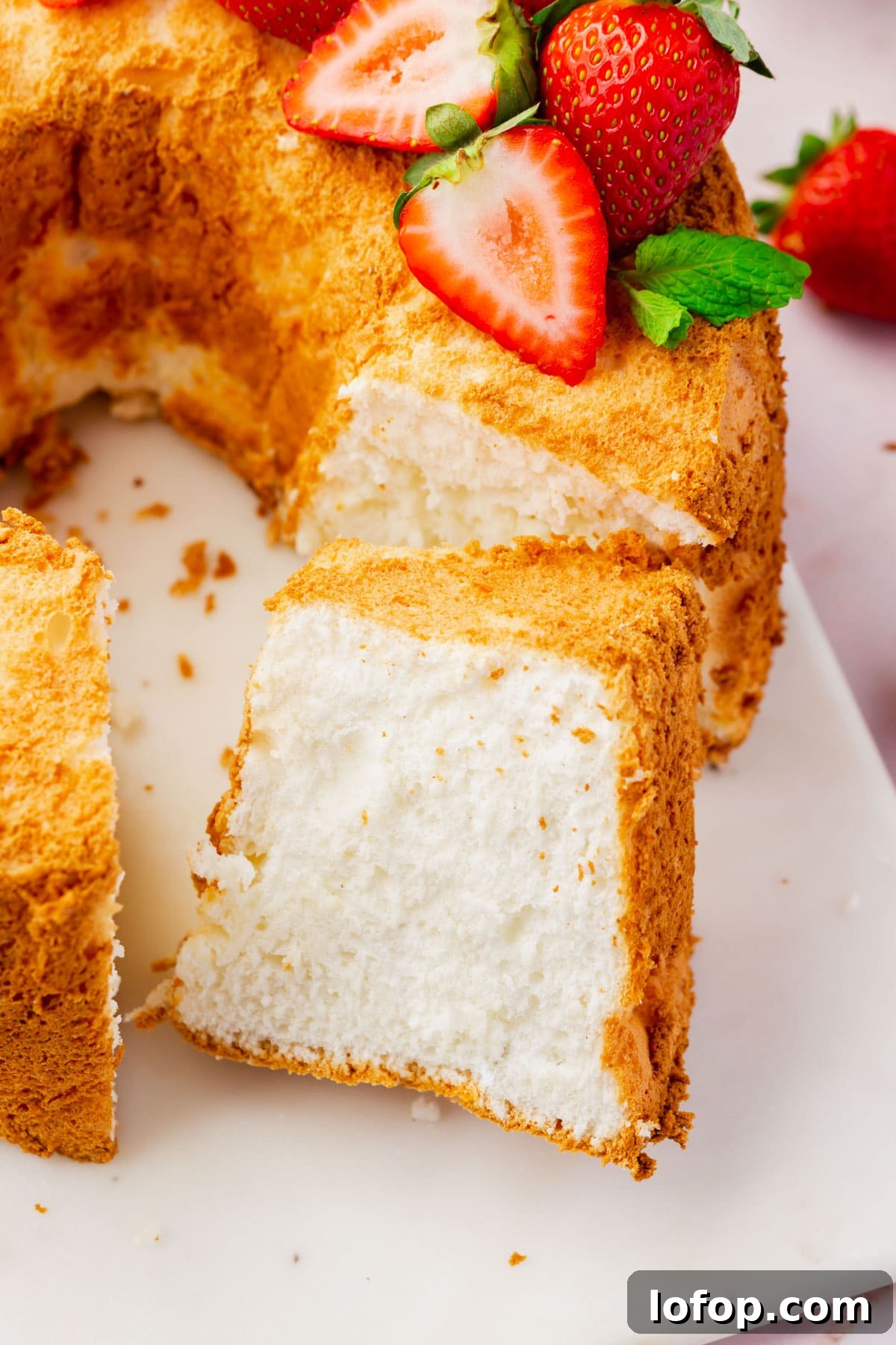 Fluffy Gluten-Free Angel Food Cake Recipe for Light Desserts 4 A close up of a slice cut off from a gluten-free angel food cake topped with strawberries.