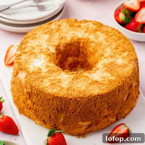 Fluffy Gluten-Free Angel Food Cake Recipe for Light Desserts 6 A gluten-free angel food cake on a marble board with fresh strawberries, a bowl of mint leaves and a bowl of whipped cream.