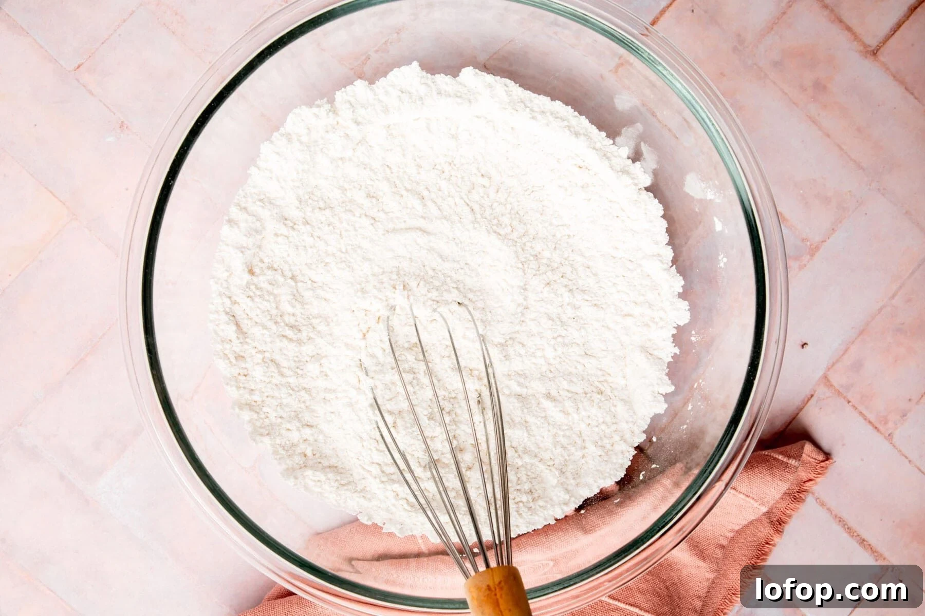 Gluten-free flour and powdered sugar in a glass mixing bowl with a whisk.