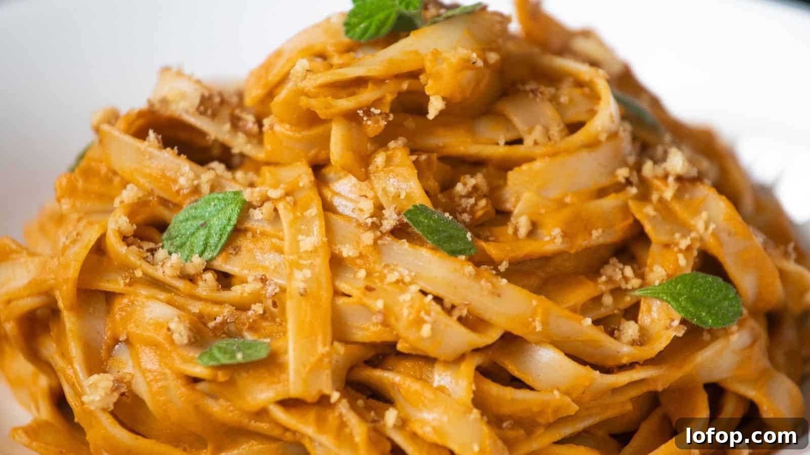 31 Budget-Friendly Winter Meals to Stretch One Grocery Trip Into a Week 13 A close-up of tagliatelle pasta coated in a creamy orange sauce, topped with chopped nuts and fresh green herbs.