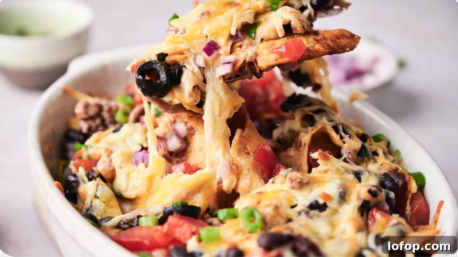 31 Budget-Friendly Winter Meals to Stretch One Grocery Trip Into a Week 18 A bowl of taco casserole topped with melted cheese, black olives, tomatoes, and green onions, with a creamy dip in the background.