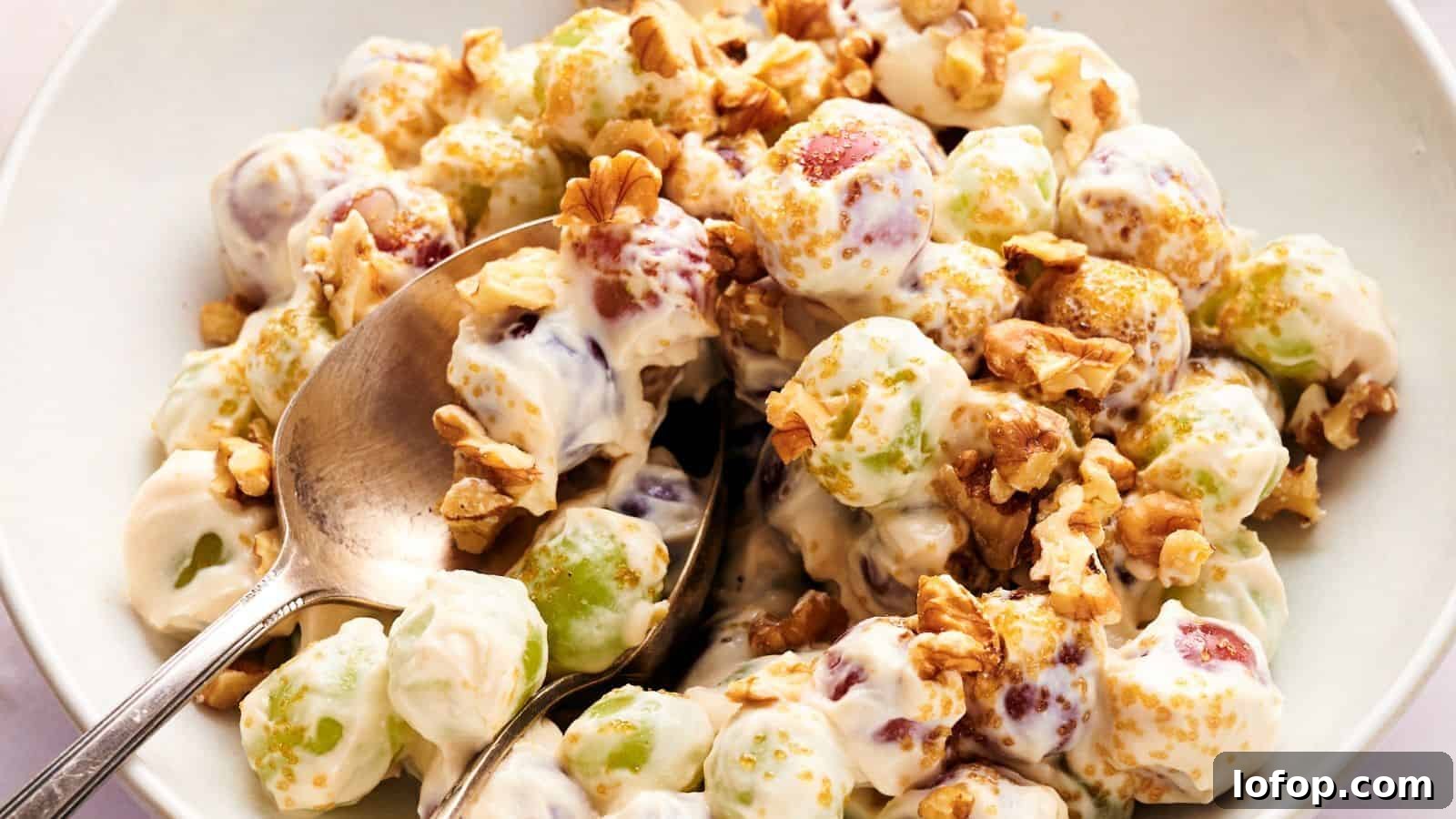 31 Budget-Friendly Winter Meals to Stretch One Grocery Trip Into a Week 25 A bowl of grape salad with green and red grapes coated in creamy dressing, topped with chopped walnuts and brown sugar, with a spoon for serving.