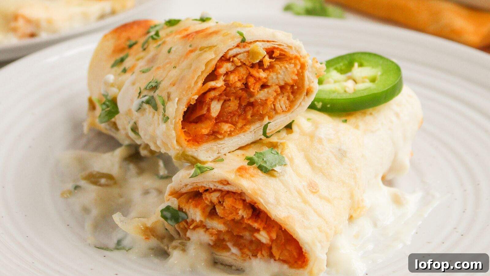 31 Budget-Friendly Winter Meals to Stretch One Grocery Trip Into a Week 28 Two tortilla-wrapped enchiladas filled with shredded chicken, topped with creamy white sauce, chopped cilantro, and a jalapeño slice, served on a white plate.