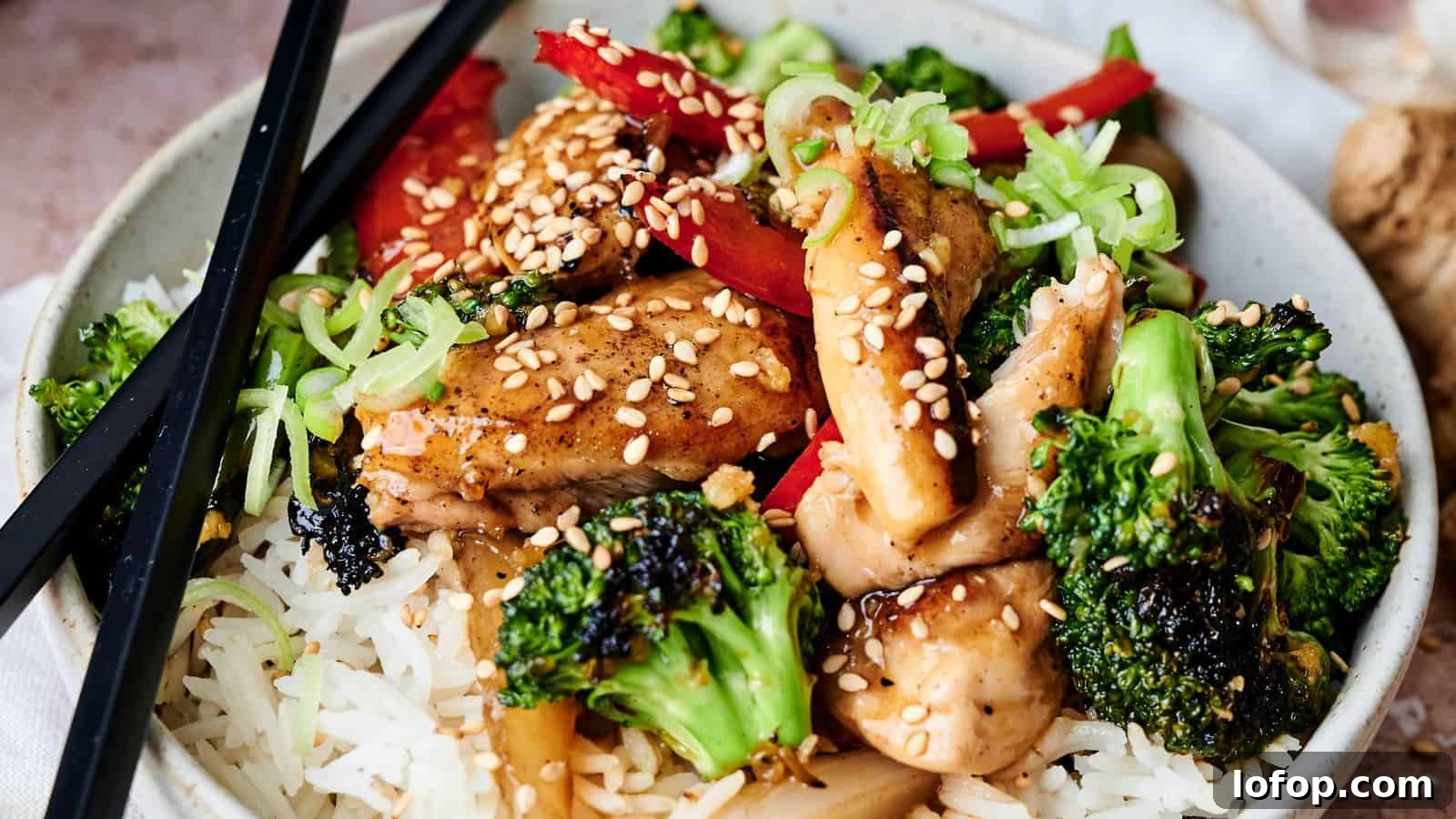 31 Budget-Friendly Winter Meals to Stretch One Grocery Trip Into a Week 30 A bowl of rice topped with broccoli, chicken, red peppers, green onions, and sesame seeds, with black chopsticks resting on the side.
