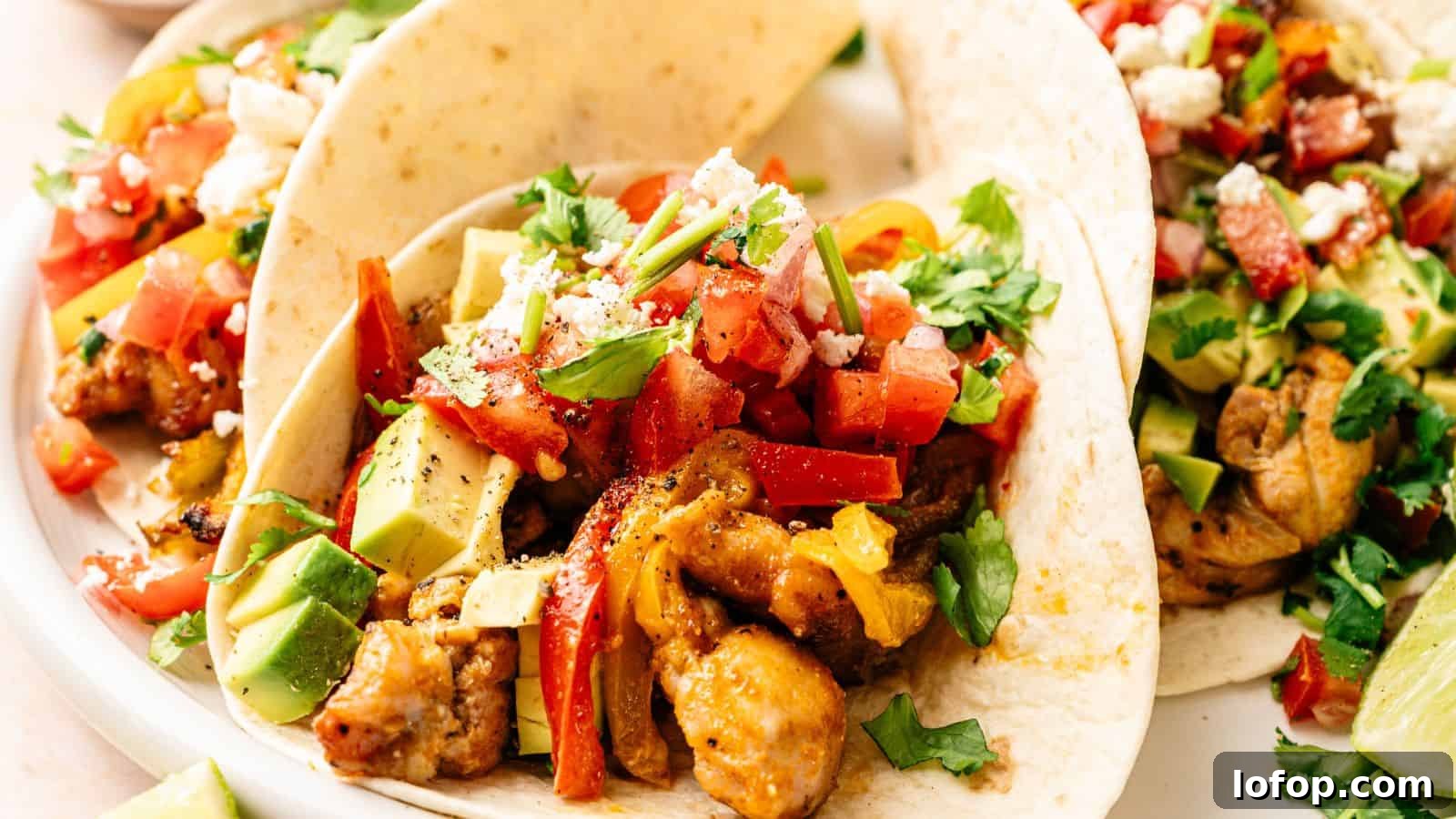 31 Budget-Friendly Winter Meals to Stretch One Grocery Trip Into a Week 32 Three soft tacos filled with seasoned chicken, diced avocado, chopped tomatoes, crumbled cheese, and fresh cilantro on a white plate.
