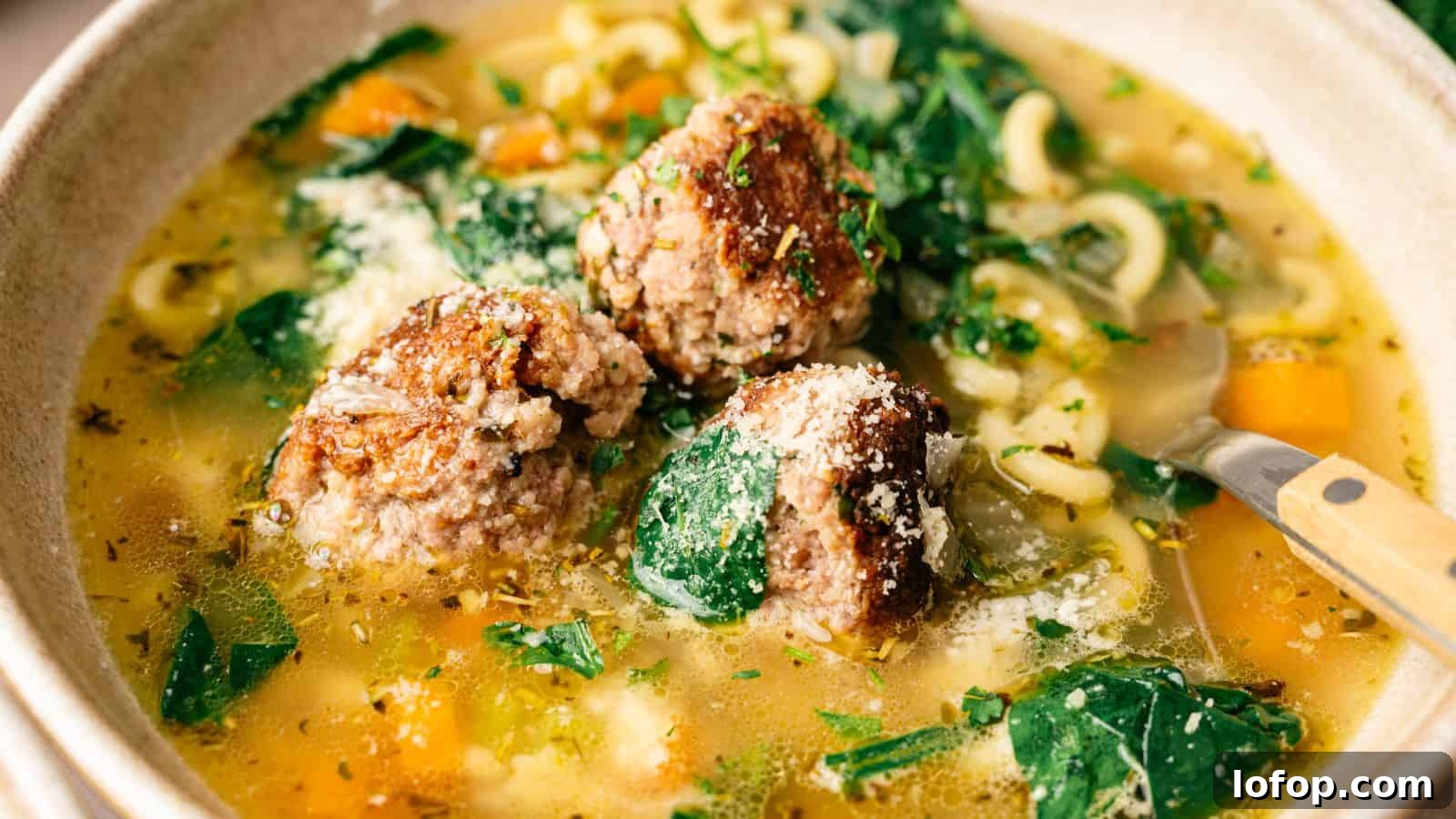 31 Budget-Friendly Winter Meals to Stretch One Grocery Trip Into a Week 8 Bowl of soup with meatballs, spinach, pasta, and vegetables in broth, topped with grated cheese and herbs.
