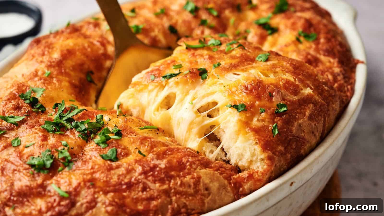 31 Budget-Friendly Winter Meals to Stretch One Grocery Trip Into a Week 9 A golden-brown baked dish with melted cheese and chopped herbs, being served with a spoon from an oval white casserole dish.