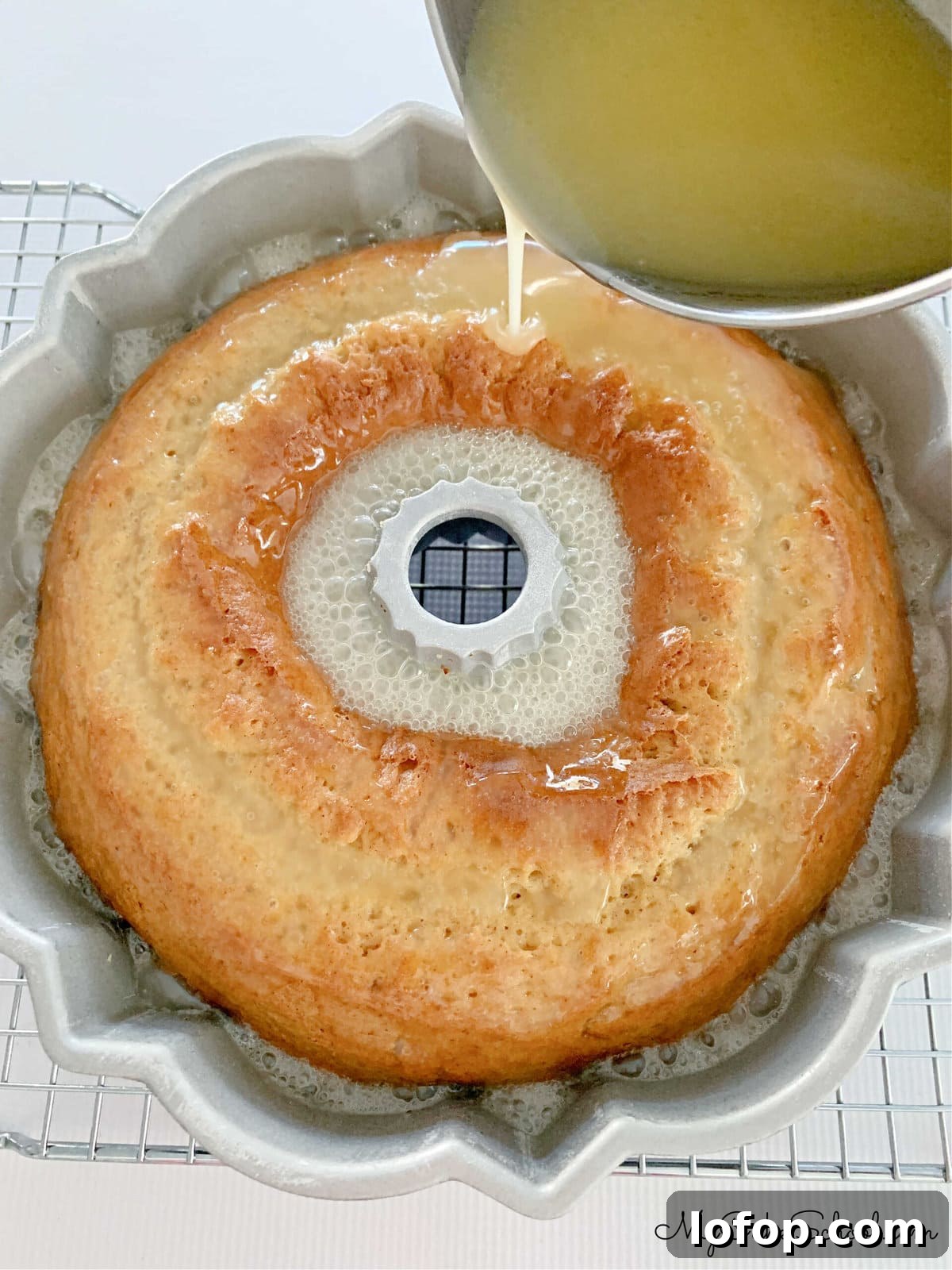 Pouring buttered rum glaze over the freshly baked cake, still in bundt pan.