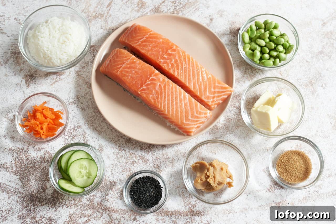 Miso Butter Salmon Rice Bowl Recipe 3 A plate with two salmon filets surrounded by small bowls of rice, edamame, grated carrots, sliced cucumbers, miso, butter, brown sugar, and black sesame seeds.