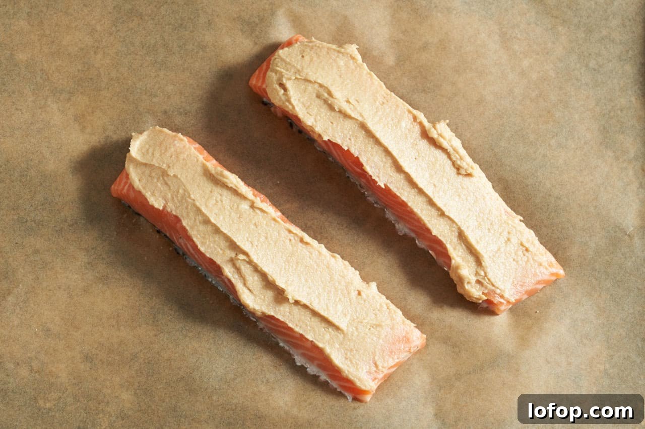 Miso Butter Salmon Rice Bowl Recipe 5 Two salmon filets with miso butter spread on top on parchment paper.