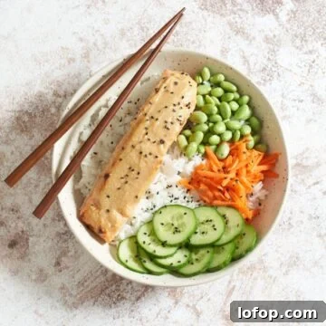 Miso Butter Salmon Rice Bowl Recipe 7 Miso butter salmon in a bowl with rice, edamame, carrots, and cucumber, topped with black sesame seeds, chopsticks rest on the left side of the bowl.