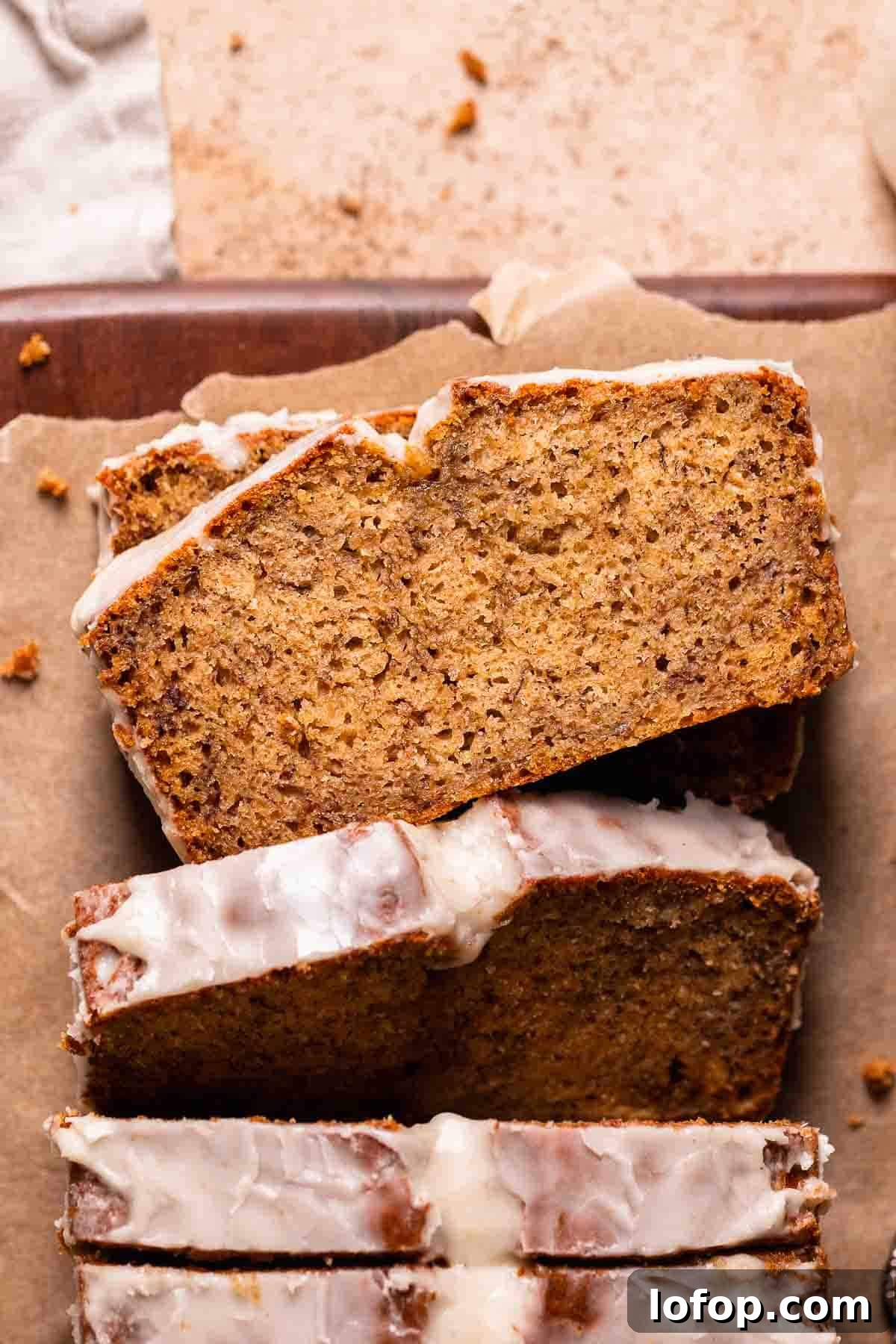 A loaf of brown butter banana bread on brown parchment paper with a slice laying flat to show the moist texture.