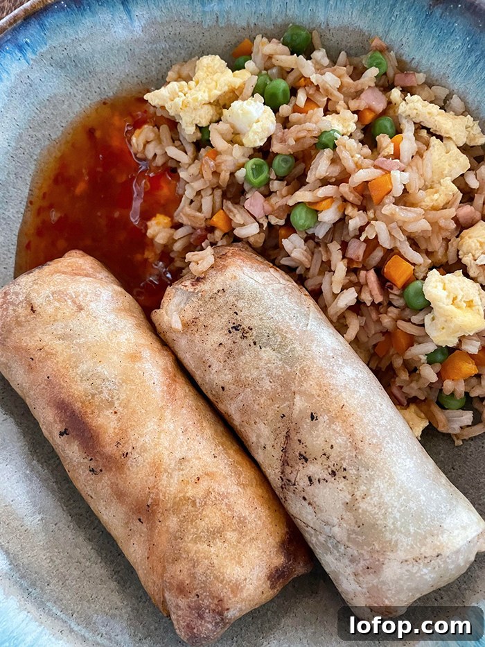 A dinner plate with two egg rolls, sweet chili sauce, and a serving of fried rice.