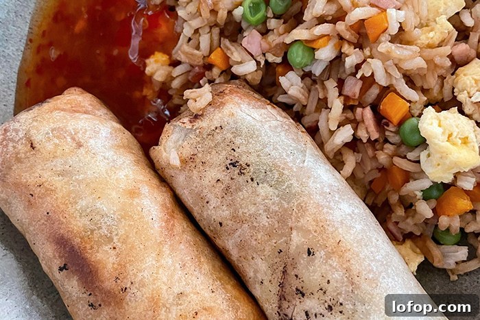 Two egg rolls, sweet chili sauce, and a serving of fried rice on a plate.