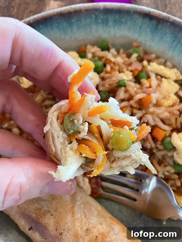 A bite of egg roll held above a plate with a serving of fried rice, a fork head, and one and a half egg roll.