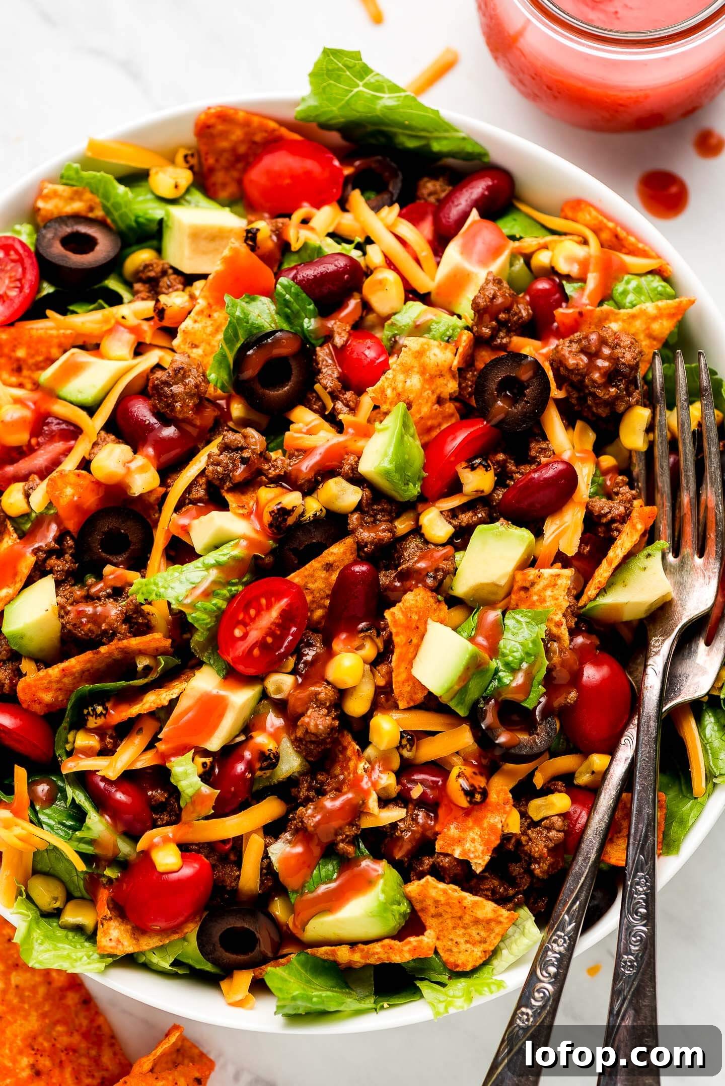 Crispy Dorito Taco Salad Recipe for Game Day and Weeknight Meals 2 Close up shot of Dorito Taco Salad drizzled with Catalina dressing and two forks in the side.