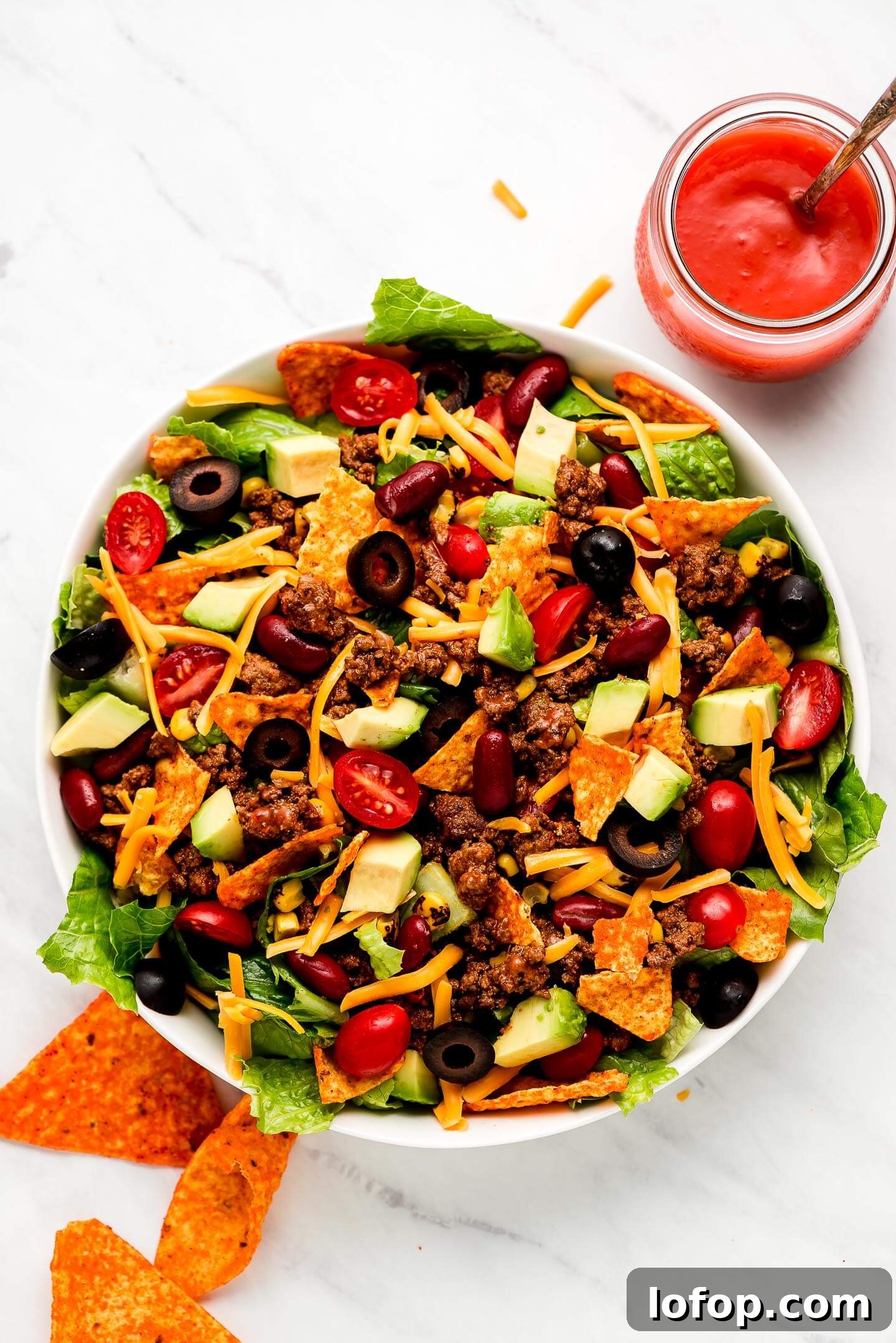 Crispy Dorito Taco Salad Recipe for Game Day and Weeknight Meals 3 A large bowl full of Dorito Taco Salad with a jar of Catalina dressing to the side.