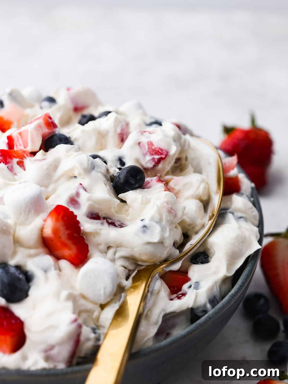 Red White and Blue Cheesecake salad being scooped up with a gold spoon.