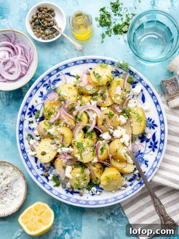 Slow Cooker Leg of Lamb with Garlic and Herbs 10 A bowl of Greek potato salad with red onions, feta cheese, herbs, and capers on a blue-patterned plate, surrounded by lemon, salt, pepper, oil, and a striped serviette on a blue table.