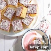Squares of jam and coconut sponge on a white plate alongside a slice served with pink custard.