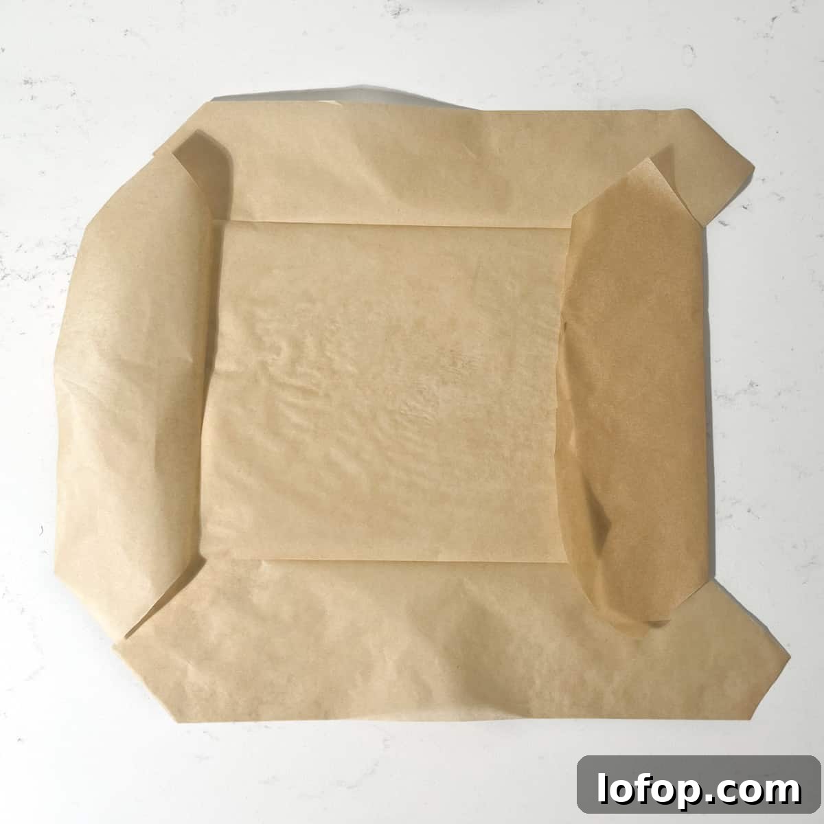 A piece of baking paper being folded on the seams before fitting it to the baking tin.
