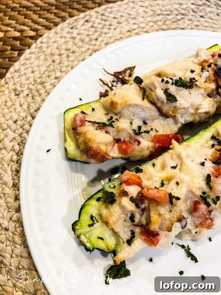 Two low carb chicken alfredo zucchini boats garnished with fresh herbs on a white plate