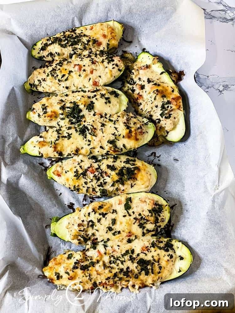 8 cooked zucchini boats with a chicken alfredo filling topped with melted cheese on a baking sheet lined with parchment paper