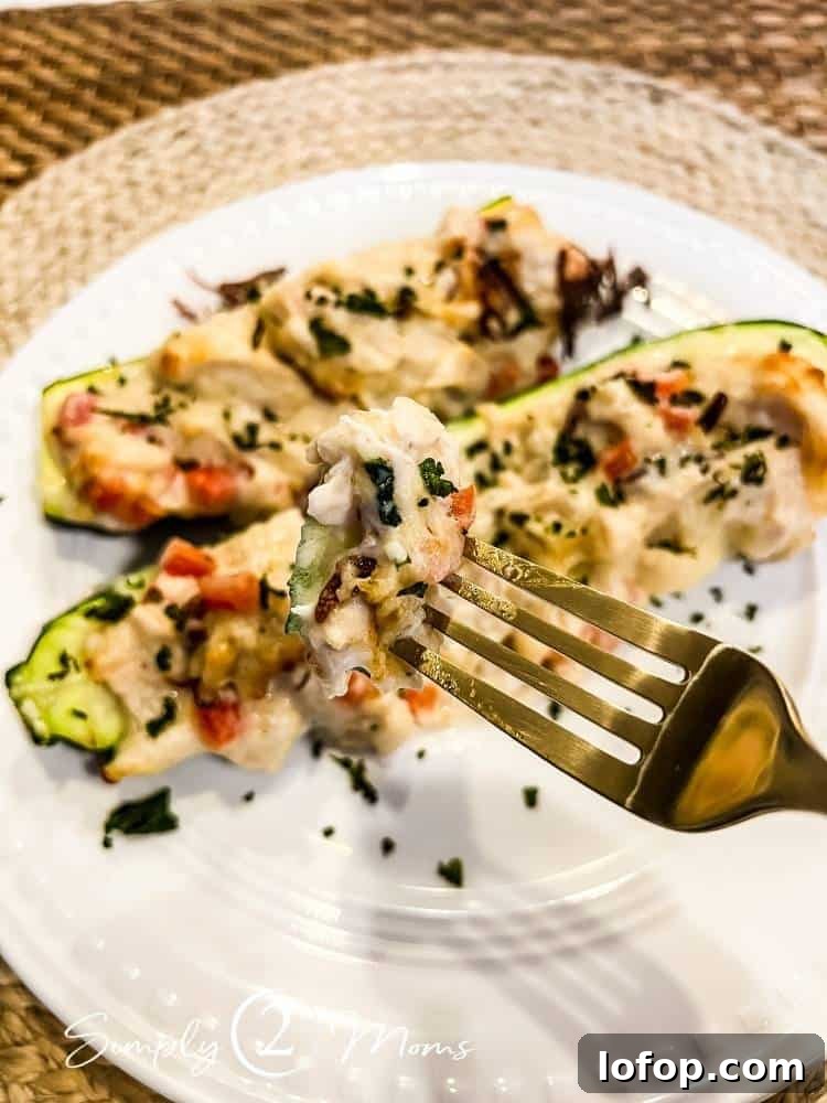 Fork with a mouthful of chicken alfredo zucchini above a plate with two low carb zucchini boats on it.