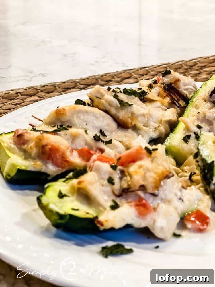 Close up of two keto chicken alfredo zucchini boats sprinkled with fresh herbs on a white plate