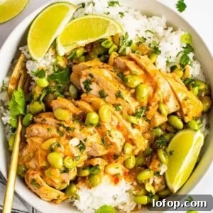 A bowl of skillet-cooked coconut chicken served over white rice, garnished with edamame beans, chopped herbs, and lime wedges.
