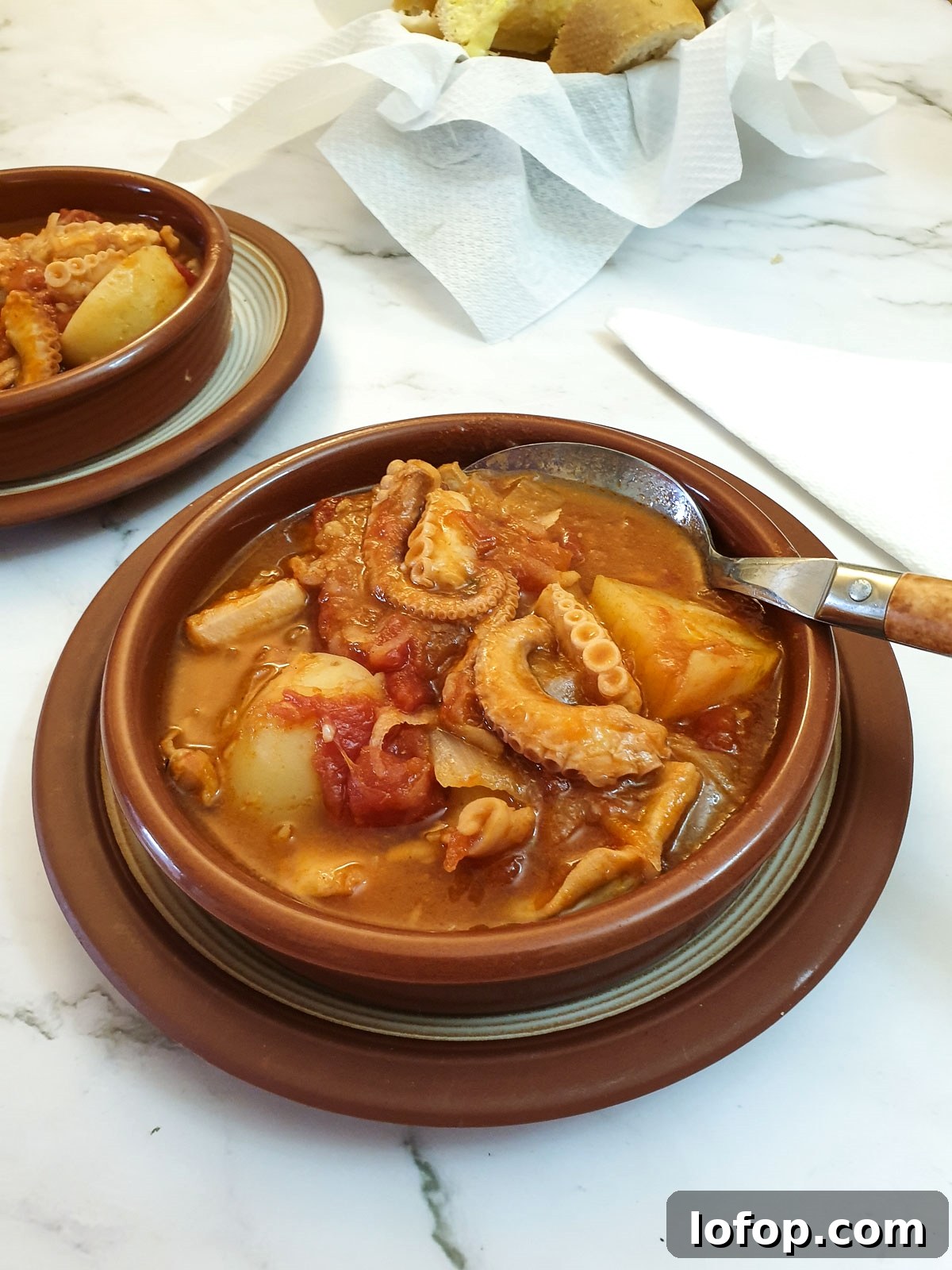 Octopus stew in tapas dishes next to a bowl of crusty bread.