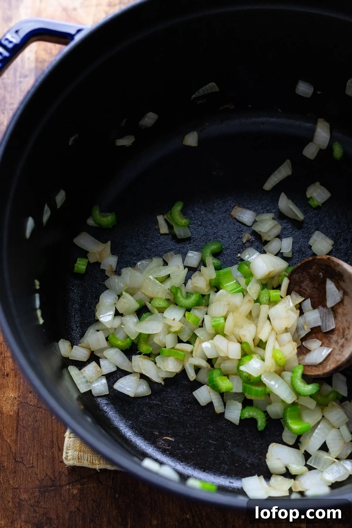 Hearty Vegetarian Black Bean Tortilla Soup Recipe 4 Diced onions and celery being sautéed in a black cast iron pot with a wooden spoon.