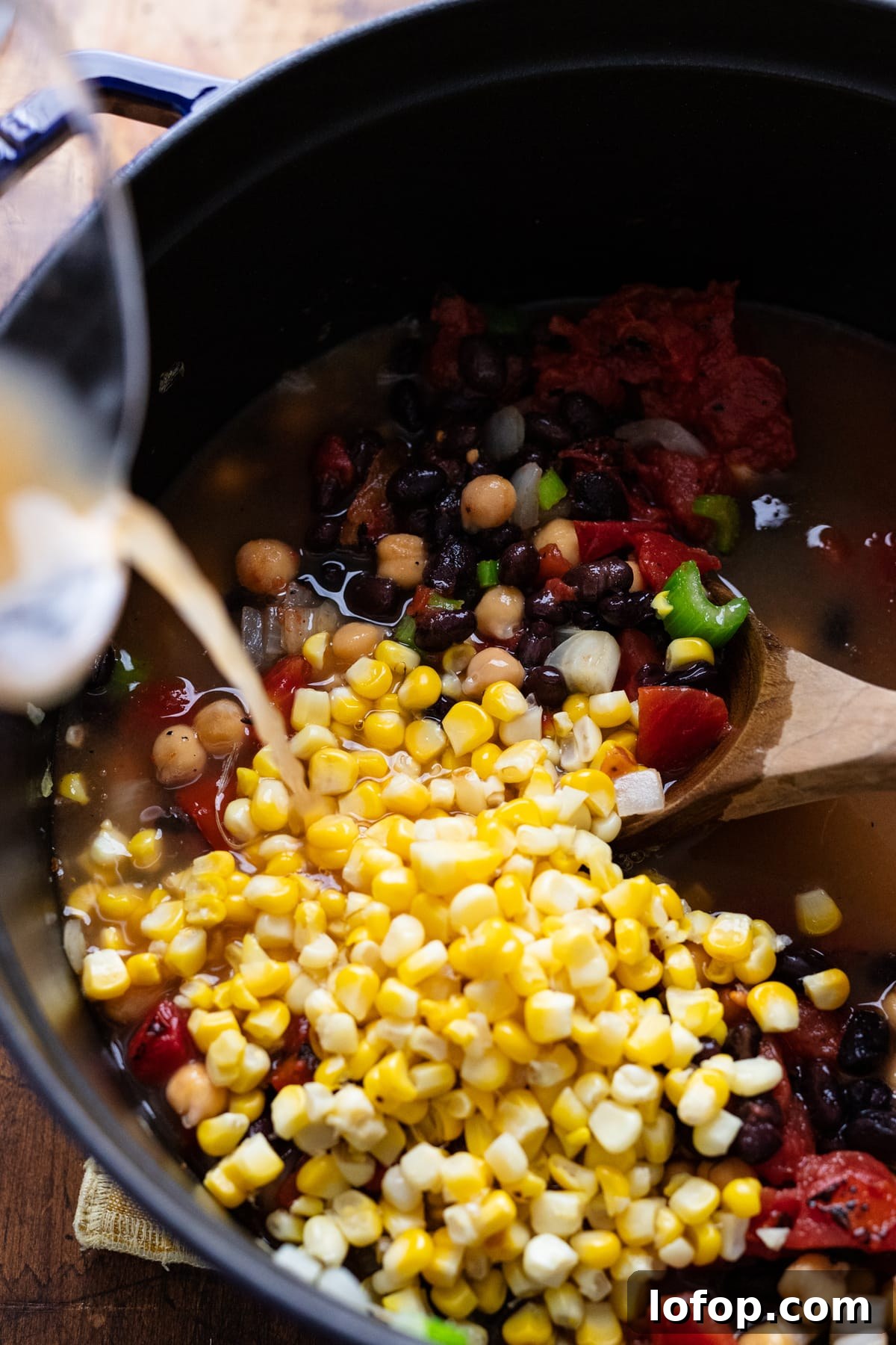 Hearty Vegetarian Black Bean Tortilla Soup Recipe 5 Broth being poured into a black pot with corn and beans in it.